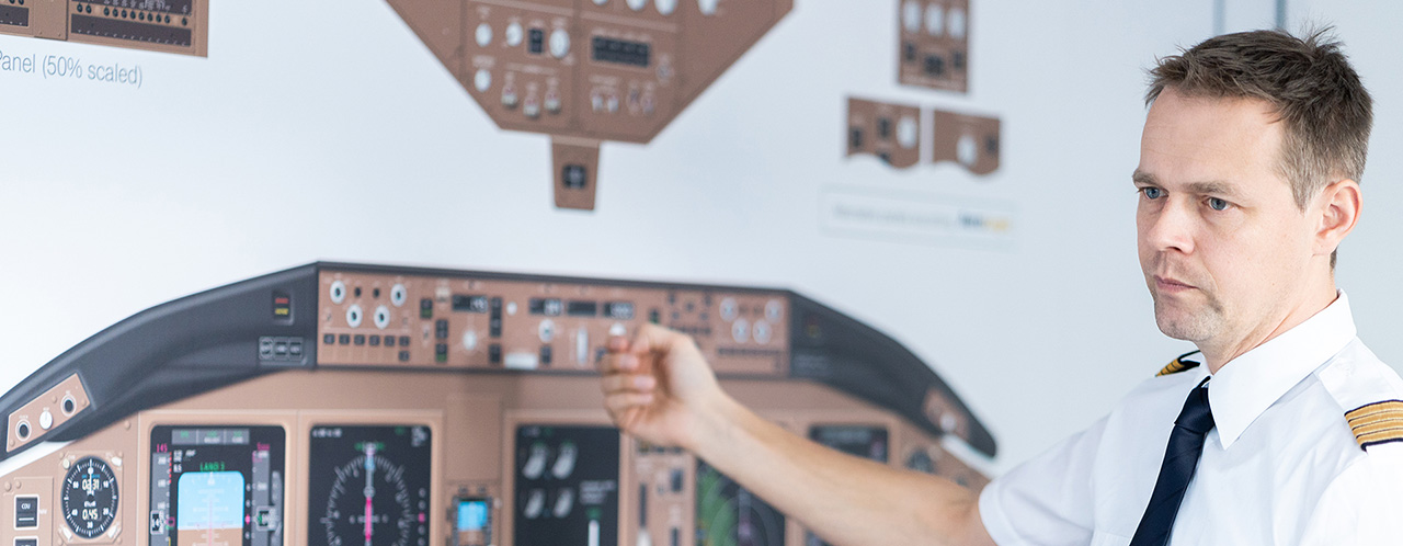 A pilot stands in front of a board showing an aircraft cockpit