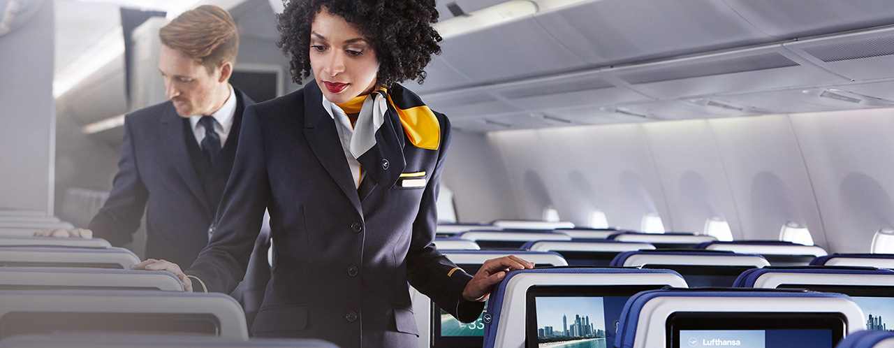 Two cabin crew members check the rows of seats in an aircraft without passengers