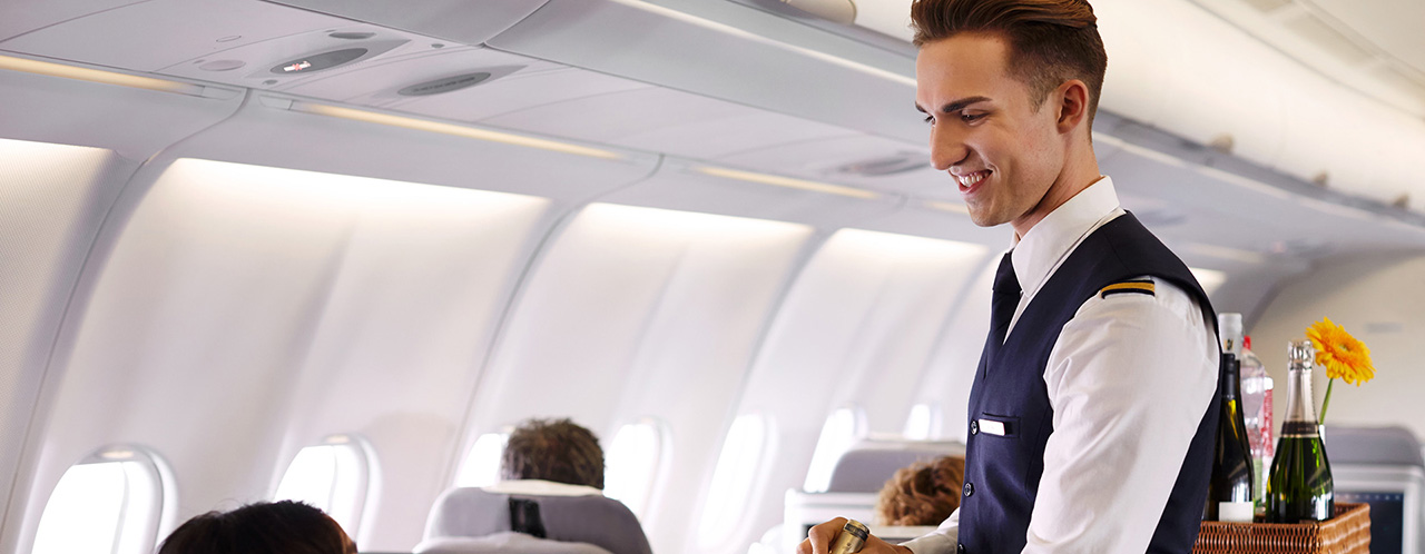 Ein Cabin Crew Mitarbeiter präsentiert einem Fluggast eine Flasche Wein