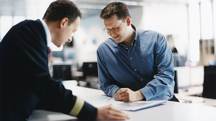 Two men, one of them a pilot in uniform, look at documents together